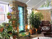 Зимний сад в загородном особняке оформлен растениями и декоративной водной панелью с подсветкой
